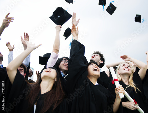 Obraz na plátně Group of diverse grads throwing caps up in the sky