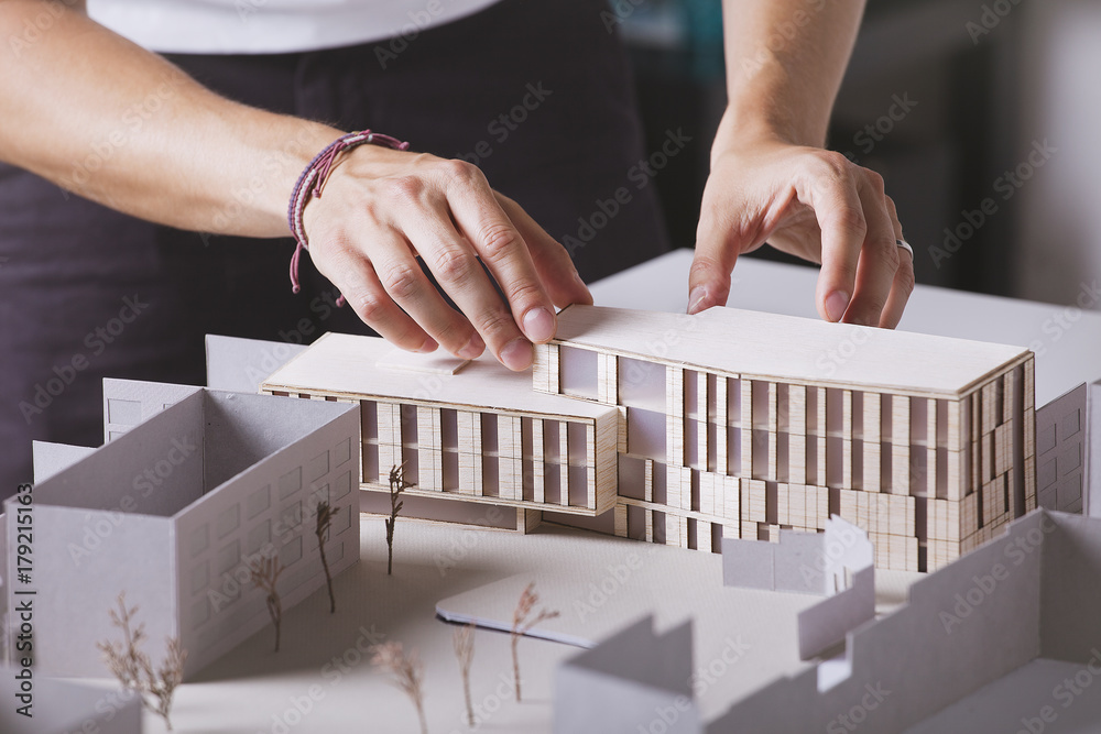 © BONNINSTUDIO/Stocksy - Close up of hands of young architect working on a building project with a scale model.