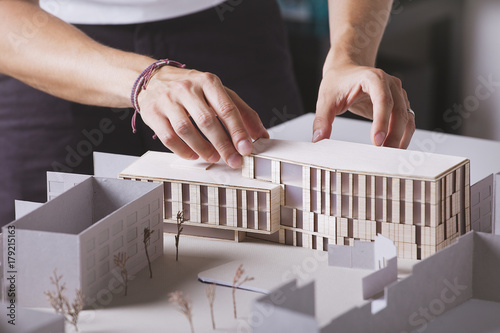 Close up of hands of young architect working on a building project with a scale model.