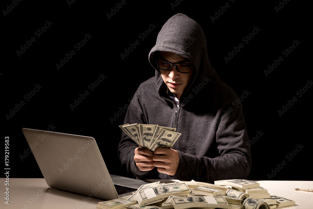 Hacker in a hood stealing information with computer on dark background Hacker in a hood stealing information with computer on dark background