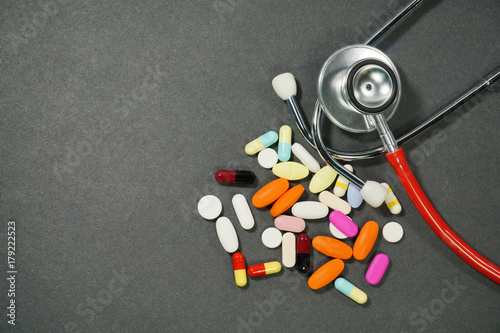 A various medicine pills and tablets and a statoscope on a black background. 