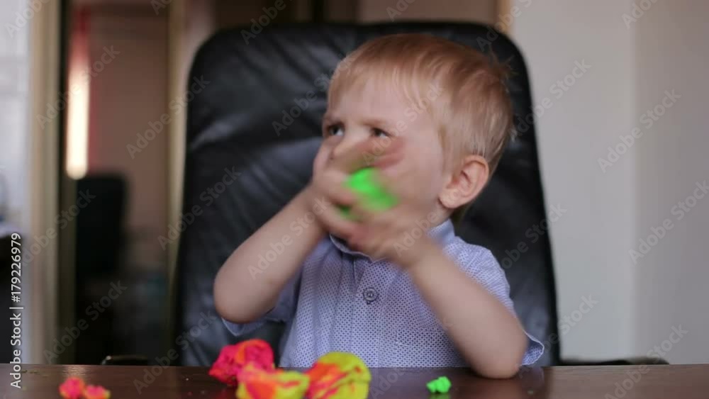 Sad little boy playing with colorful plasticine. Little boy playing with plasticine while sitting at table at home. Sad little boy playing with colorful plasticine. Little boy playing with plasticine while sitting at table at home.
