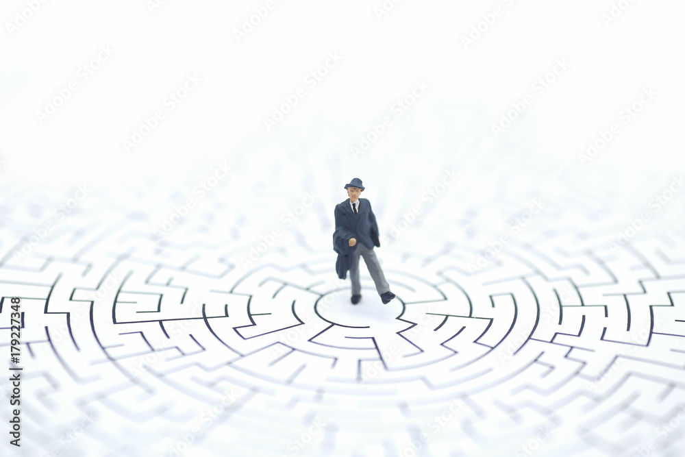 Miniature people: Businessman standing on center of maze Miniature people: Businessman standing on center of maze