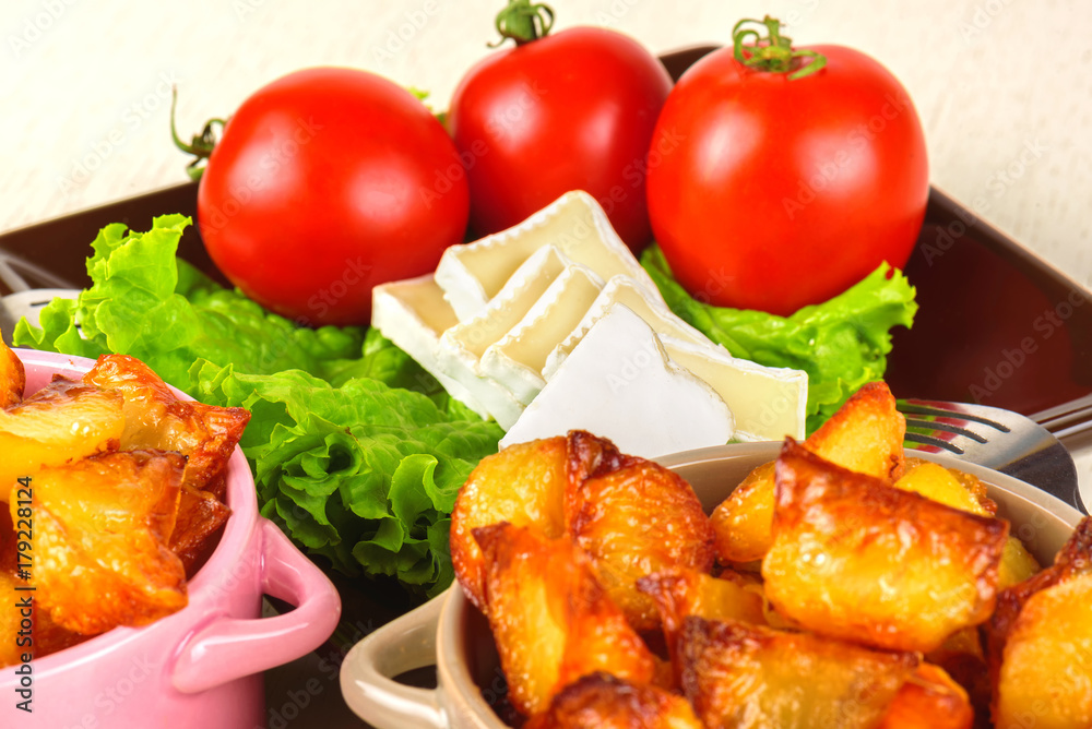 Breakfast from cheese, tomatoes, potatoes and all-over salad on a wooden table closeup.