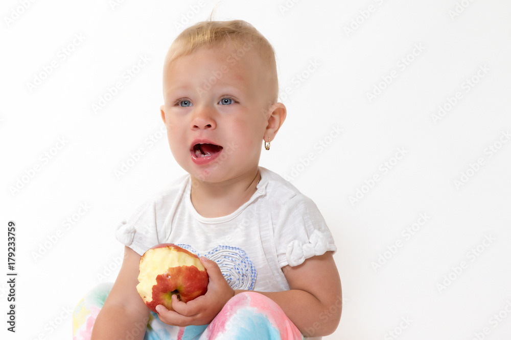 Studio shot of sitting cool toddler girl holding red apple and looking on the side of the camera with an open mouth. Studio shot of sitting cool toddler girl holding red apple and looking on the side of the camera with an open mouth.