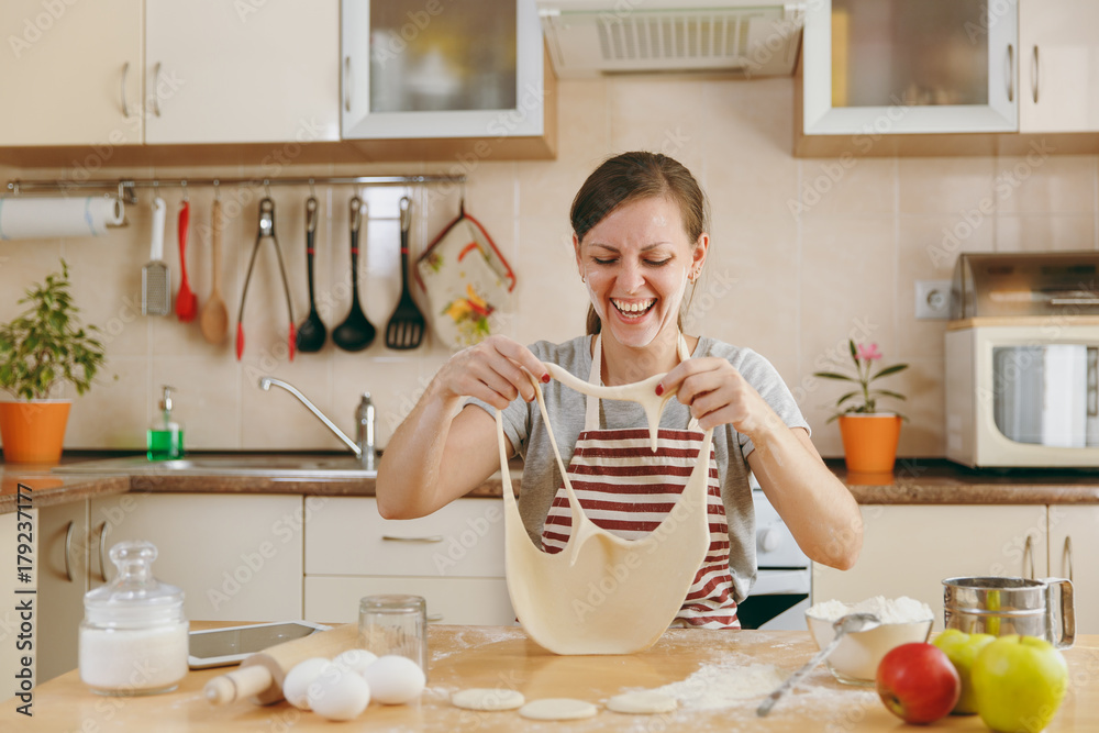 A young funny cheerful and smiling woman puts on a dough with holes on her face and has fun in the kitchen. Cooking home. Prepare food. A young funny cheerful and smiling woman puts on a dough with holes on her face and has fun in the kitchen. Cooking home. Prepare food.