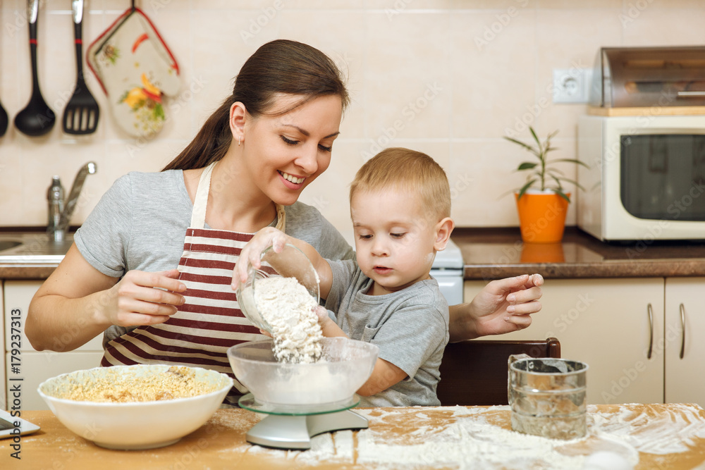 Little kid boy helps mother to cook Christmas ginger biscuit in light kitchen with tablet on the table. Happy family mom 30-35 years and child 2-3 in weekend morning at home. Relationship concept Little kid boy helps mother to cook Christmas ginger biscuit in light kitchen with tablet on the table. Happy family mom 30-35 years and child 2-3 in weekend morning at home. Relationship concept