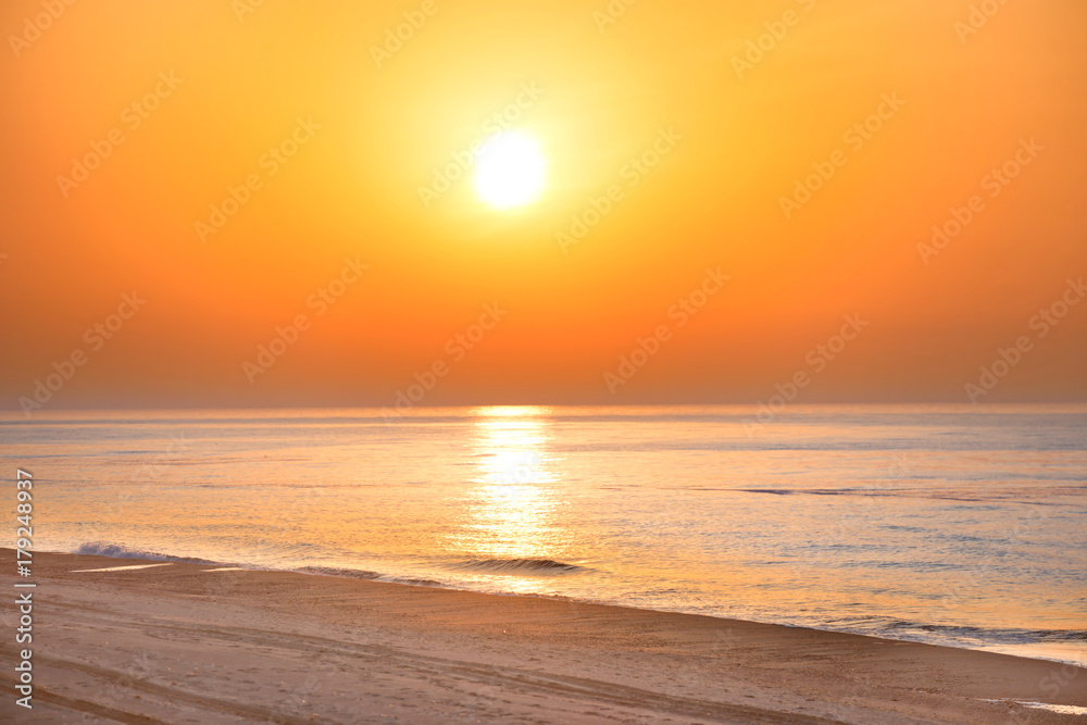 Naklejka premium Zmierzch na plaży z długą linią brzegową, słońcem i dramatycznym niebem