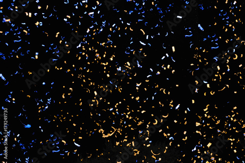 Confetti fired in the air during a beach party. Only confetti on black background of the night. Confetti blue and yellow