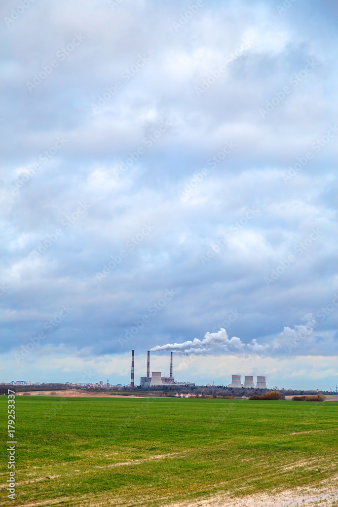 Smoking chimneys of an old factory on the background of green grass and autumn sky in the clouds