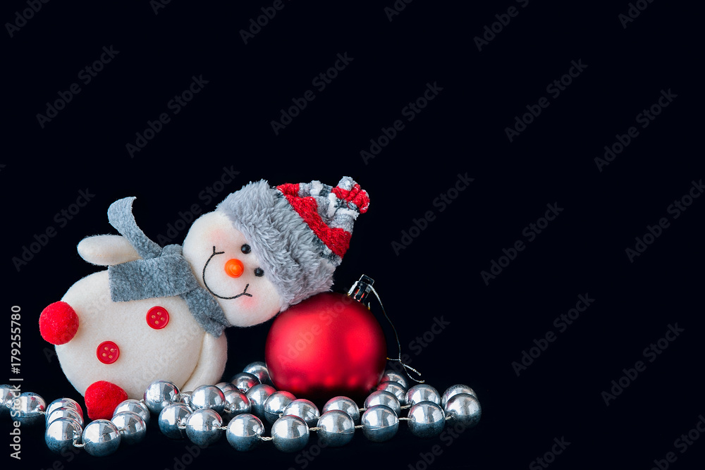 Happy cute smiling  toy snowman in hat and scarf with balls, garland and Christmas tree on a black background.Red, white and silver color. Christmas and New Year 2018 celebration.