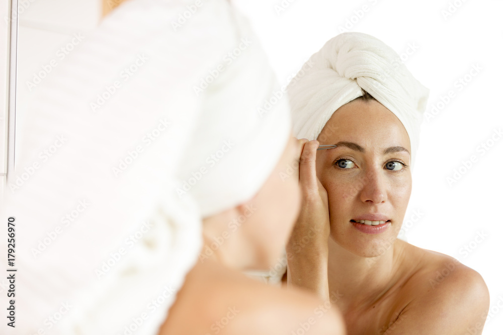 Woman shaping of her eyebrows with tweezers looking in mirror Woman shaping of her eyebrows with tweezers looking in mirror