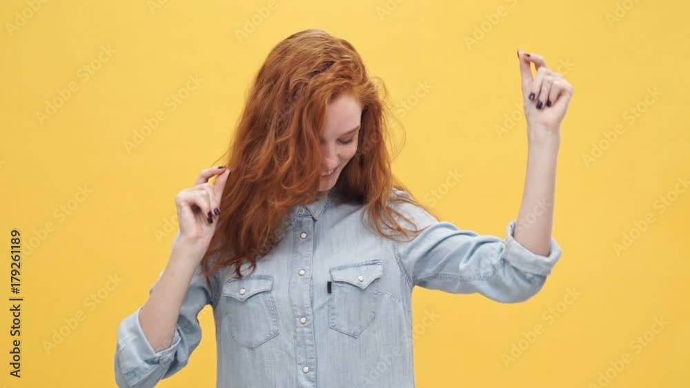 Happy ginger woman in denim shirt dancing and looking at the camera over yellow background
Happy ginger woman in denim shirt dancing and looking at the camera over yellow background