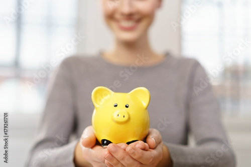 glückliche frau hält ein kleines gelbes sparschwein in den händen