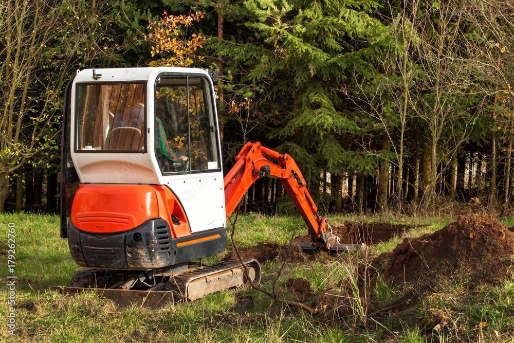 Work on the construction site of an ecological house. The excavator adjusts the terrain. A small digger in the garden. Work on the construction site of an ecological house. The excavator adjusts the terrain. A small digger in the garden.