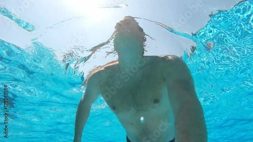 Young man swimming in pool and holding camera in hand. Underwater footage. Slow motion