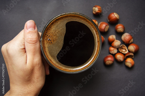 Hand holds a cup of hot coffee with foam against the hazelnut