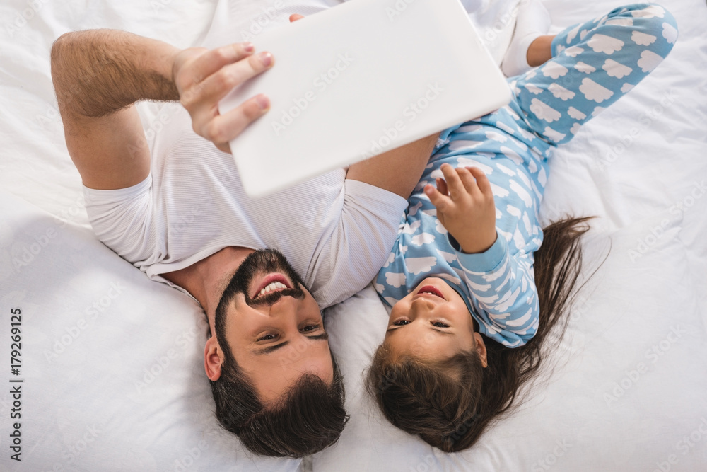 father and daughter using tablet in bed