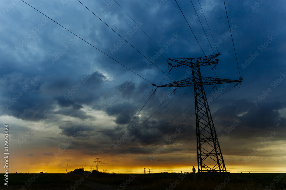 High voltage power lines and transmission towers at sunset. Poles and overhead power lines silhouettes in the dusk. Electricity generation and distribution. Electric power industry and nature concept