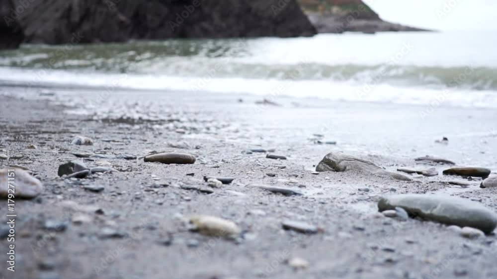 Low down angle looking out to see across a pebble and sand beach, with waves crashing in slow motion Low down angle looking out to see across a pebble and sand beach, with waves crashing in slow motion