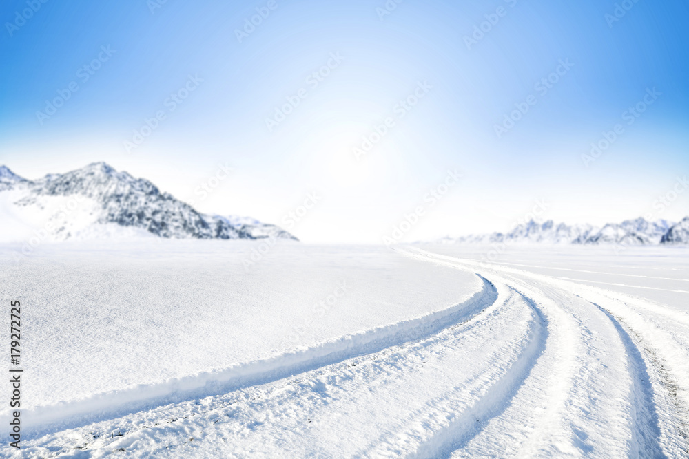 Winter Background of foreground of road covered with snow and ice. In the background, the arctic landscape of the mountains with the beautiful blue sky. Winter Background of foreground of road covered with snow and ice. In the background, the arctic landscape of the mountains with the beautiful blue sky.
