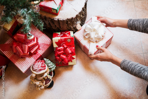 Close up of woman hands putting down a gift box under a Christmas tree.