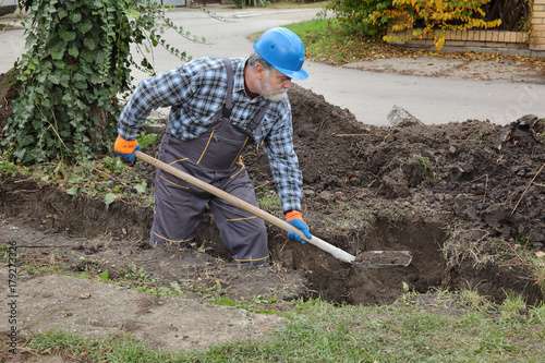 Construction worker digging trench using shovel, hole for wall foundation or pipeline  photo