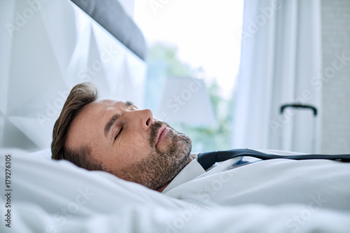 Close up of tired businessman napping in hotel room bed after travelling on business trip
