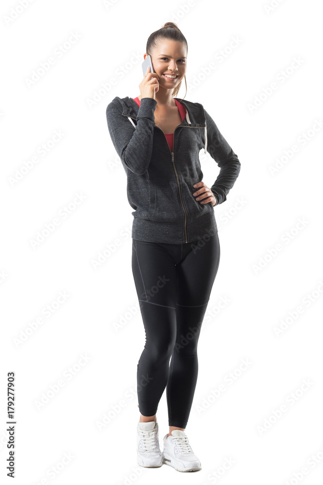 Happy smiling young fit woman in sports clothing talking on the phone looking at camera. Full body length portrait isolated on white background. Happy smiling young fit woman in sports clothing talking on the phone looking at camera. Full body length portrait isolated on white background.