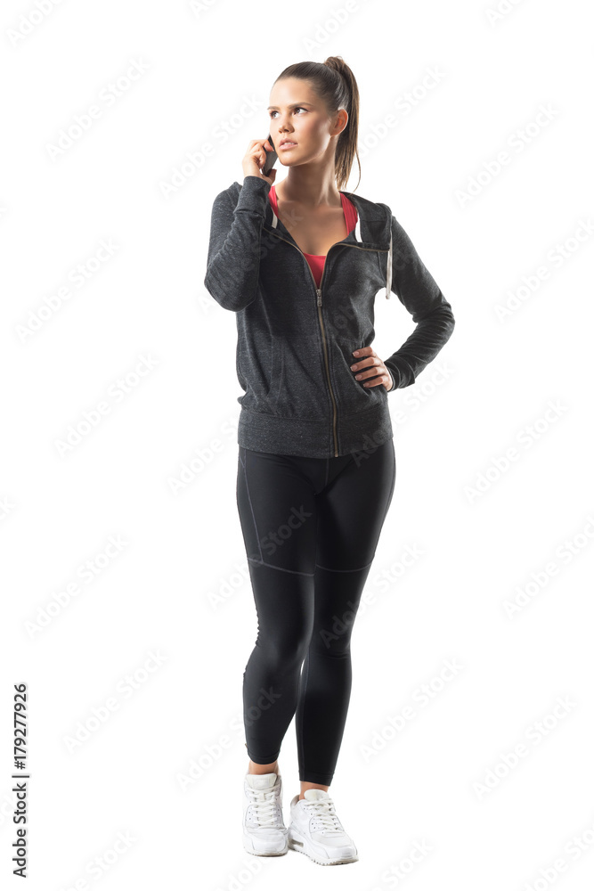 Gorgeous confident young fit female athlete talking on the phone looking up. Full body length portrait isolated on white background. Gorgeous confident young fit female athlete talking on the phone looking up. Full body length portrait isolated on white background.