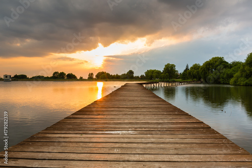 Wooden pier, bridge over lake at dramatic sunset with stormy clouds. Kuchyna, Slovakia. Landscape.