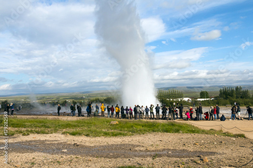 Iceland landscape - geyser valley - hot steaming geothermal sources, people walking and watching geologic features. Geyser eruption. People watching.
