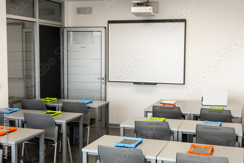 Modern classroom interior, with white board, work desks and chairs.