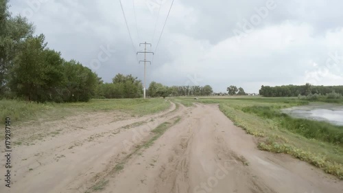 A view of the rural dirt road from camera installed on back of the car driving along this country road. Riding on a rough roadway. High voltage power line pylon. Traces of tires on the sand.