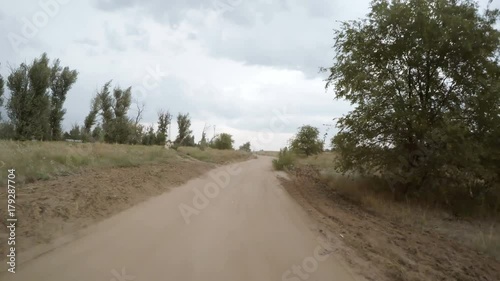 A view of the rural dirt road from camera installed on back of the car driving along this country road. Riding on a rough roadway. Traces of tires on the sand.