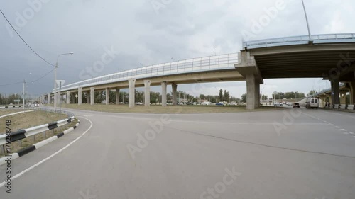 The car goes on an exit on a high speed highway, on a line of oncoming traffic other cars go. Rear view. The storm clouds in the sky.