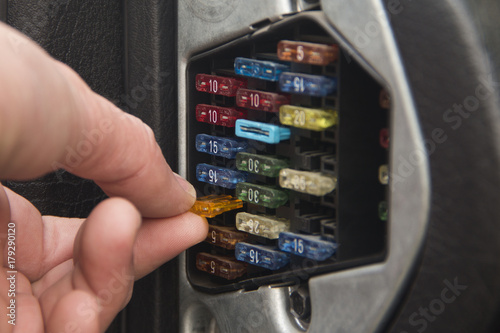 The auto mechanic inserts or pulls out the fuse from the box with the fuses of the car. photo