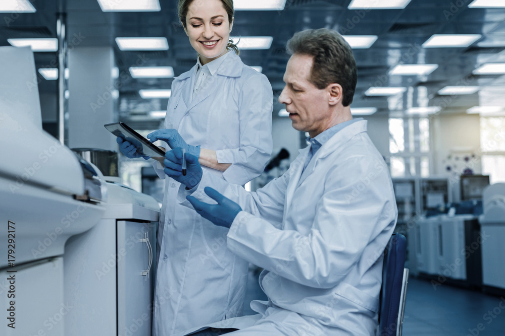 Obraz premium Scientific research. Smart handsome nice man sitting on the chair in the lab and holding a test tube while carrying out a scientific research