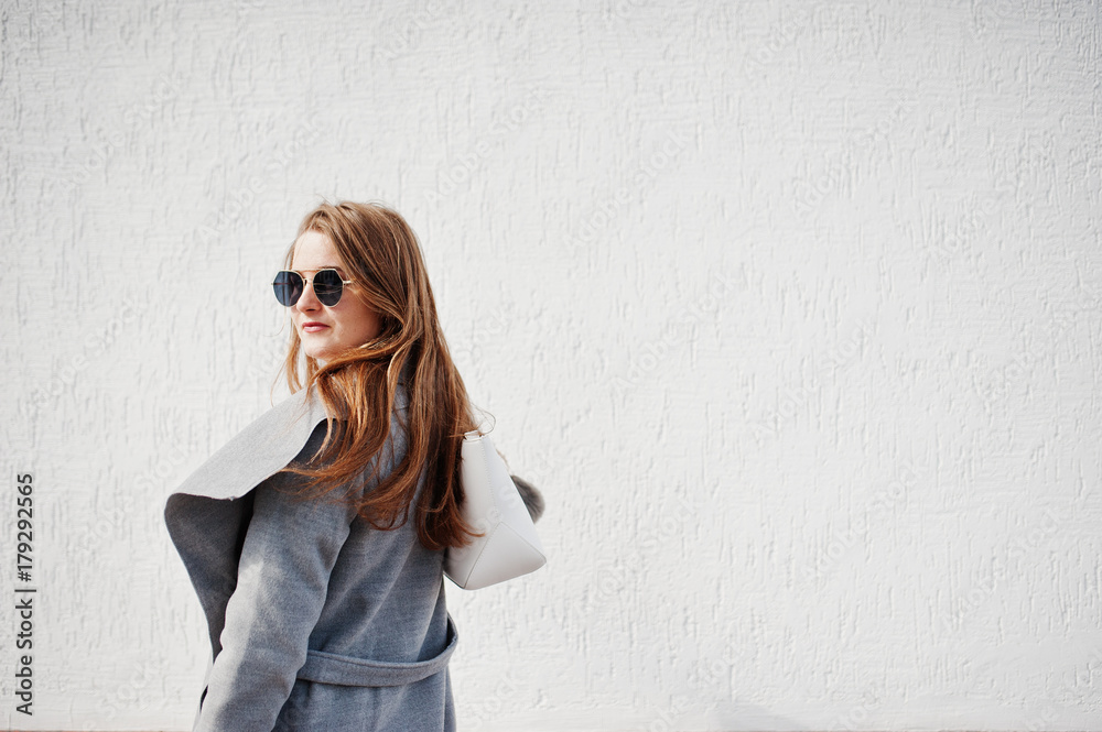 Girl in gray coat with sunglasses and handbag stay against white wall. Girl in gray coat with sunglasses and handbag stay against white wall.