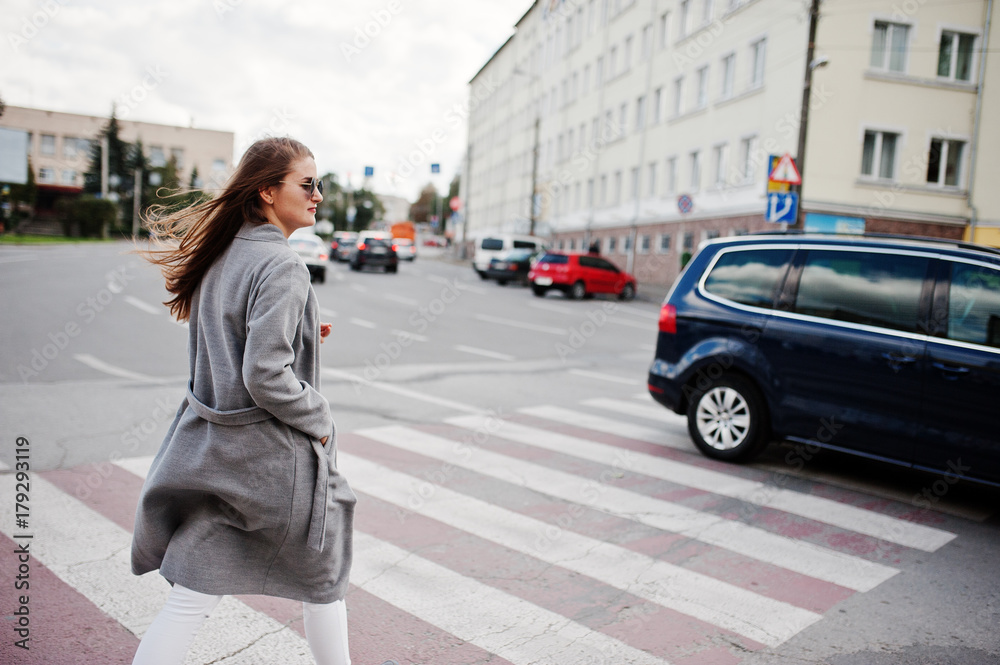 Girl in gray coat with sunglasses and handbag walking on the pedestrian crossing. Girl in gray coat with sunglasses and handbag walking on the pedestrian crossing.