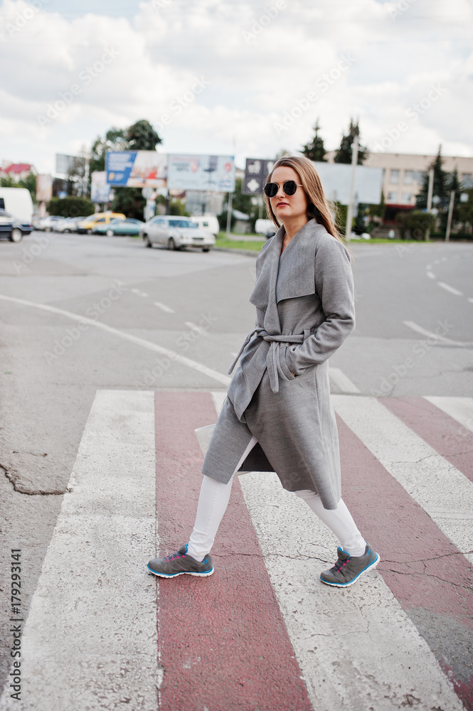 Girl in gray coat with sunglasses and handbag walking on the pedestrian crossing.