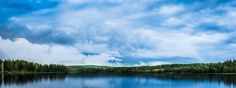 Peaceful landscape with lake, forest and spectacular, blue, cloudy sky reflecting in the water