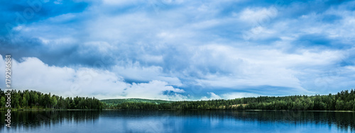 Peaceful landscape with lake, forest and spectacular, blue, cloudy sky reflecting in the water
