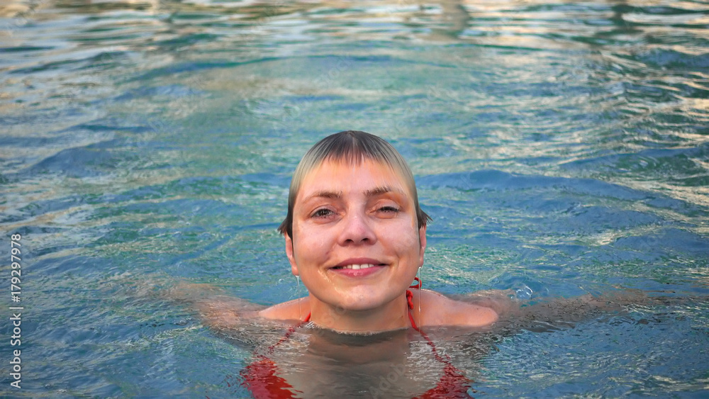 Young woman in red bikini is emerging from the water in swimming pool. Diving and coming up is good time sport recreational enjoyment in a water pool.