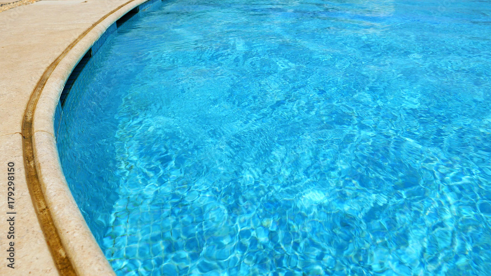 Blue water in swimming pool. Waves and patches of sunlight appears on the bottom of the pool. Glares blinks and reflections on clear water.