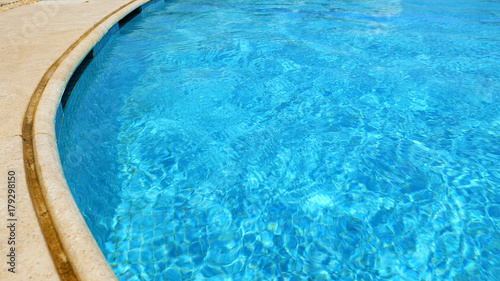 Blue water in swimming pool. Waves and patches of sunlight appears on the bottom of the pool. Glares blinks and reflections on clear water.