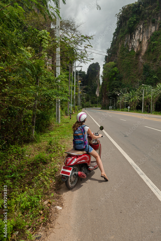 tourist woman sitting on classic scooter against the background of the mountains of Krabi Province, Thailand. tourist woman sitting on classic scooter against the background of the mountains of Krabi Province, Thailand.