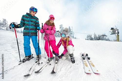 Mom with children on ski terrain preparing daughter for skiing