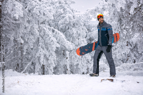 smiling man with ski mask holding his snowboard, extreme sport and winter holiday