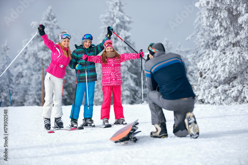 father taking picture of family on ski holiday in mountains